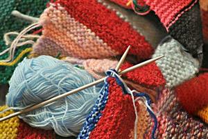 Pile of colorful striped knit fabric with a pair of needles sitting on top.